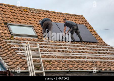 Workers installing solar panels or pv cells on the pantiled roof of a Norfolk cottage.  NB: The premises in the photograph are Property Released. Stock Photo