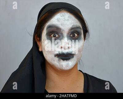 Young Mexican woman with traditional white zombie-like Catrina face make-up on the Day of the Dead (Día de los Muertos) wears black clothes. Stock Photo