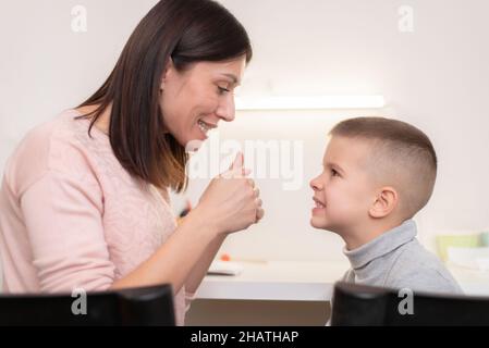 A beautiful woman speech therapist deals with the boy and teaches him the correct pronunciation and competent speech. Stock Photo