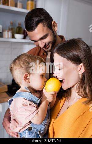 Woman biting lemon near toddler son and husband at home Stock Photo
