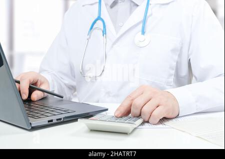 Doctor working with medical statistics and financial reports. doctor counts on calculator and enters data into laptop. doctor working with laptop and Stock Photo