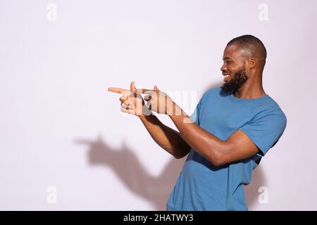 Black man with a blue t-shirt smiling and showing something on a white background. Stock Photo