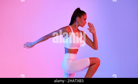 Fitness Lady Standing Doing Elbow-To-Knee Crunch Over Neon Background, Panorama Stock Photo