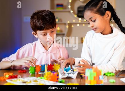Kids in concentration busy making Robotic experiment by by joining parts at home - concept of STEM Education, Childhood development, teamwork and Stock Photo