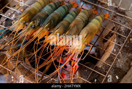 Grilled prawn on charcoal grill. Giant freshwater prawns grill on a flaming charcoal fire. Closeup giant river prawn cooking on barbecue grill rack. Stock Photo