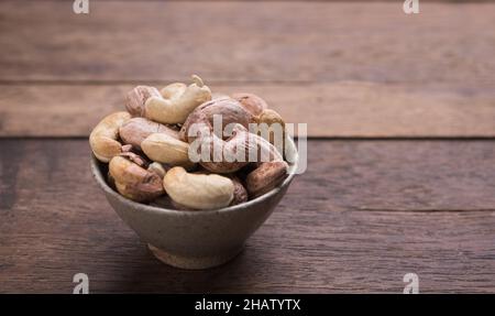 Cashews nuts with shells,homemade roasted process in ceramic bowl on wooden background Stock Photo