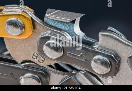 Sharp steel tooth of chainsaw chain detail on a dark blue background. Closeup of metal chain link with cutting blade. Spare part of professional tool. Stock Photo