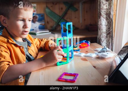 boy sits at desk and builds tower from magnetic constructor Stock Photo