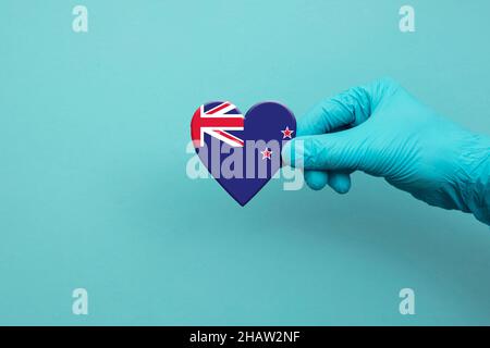 Medical workers hand wearing surgical glove holding New Zealand flag heart Stock Photo