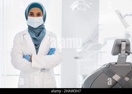 Islamic Dentist Lady Wearing Protective Medical Face Mask Posing At Worklace In Clinic Stock Photo