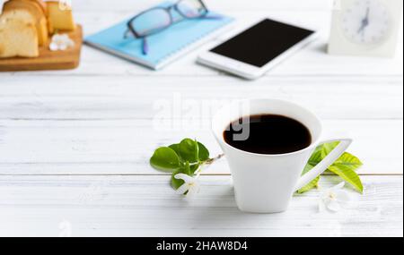Breakfast set with coffee cup,crispy butter bread,mobile phone,eye glasses,and blue notebook on white wood table Stock Photo