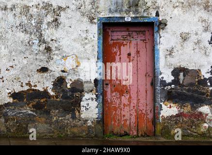 Weathered house facade with old closed red front door in Porto Formoso, Sao Miguel Island, Azores, Portugal Stock Photo