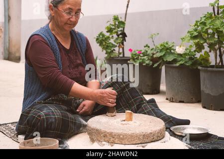 The ancient hand mill or quern stone, grinds the grain into flour. Old handmade grinding stones. The old woman is grinding flour with the traditional Stock Photo