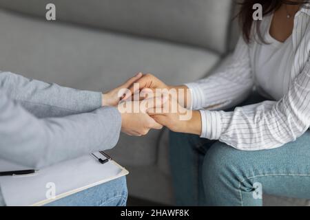 Professional compassion. Psychotherapist supporting depressed woman, holding her hands, sitting in clinic, cropped Stock Photo