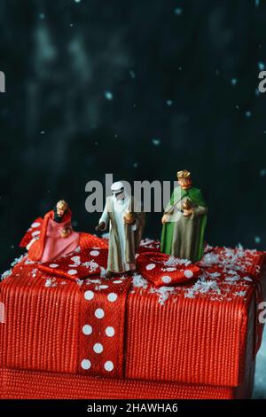 closeup of the miniatures of the magi on top of a red gift box tied with a satin red ribbon patterned with white dots, on a dark background with some Stock Photo