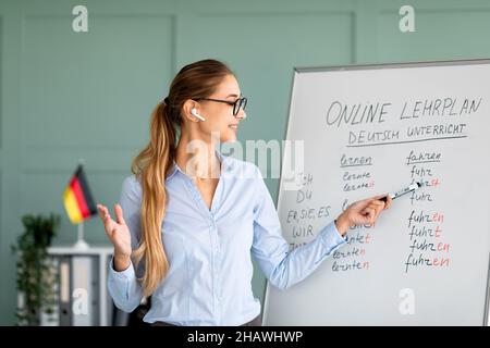 Happy German teacher explaining foreign language rules, wearing airpods, teaching linguistic online course Stock Photo