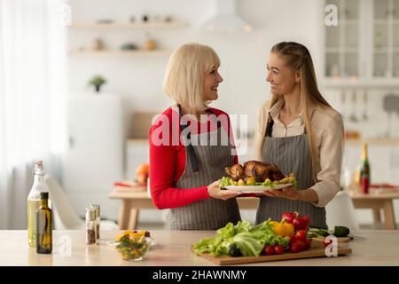 Happy young woman and her senior mother holding dish with traditional roasted Christmas turkey, cooking holiday dinner Stock Photo