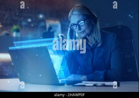 Focused mature blonde woman, executive, ceo, financial expert, stock broker, using laptop, sitting at workplace, working, analyzing financial data, doing research, planning strategy. Future technology Stock Photo