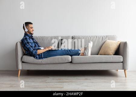 Smiling Arab man in headphones using pc at home Stock Photo