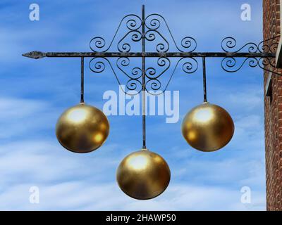 Pawn shop close up traditional sign three gold balls above Pawnbroker shop premises supported on ornamental iron bracket on a blue sky day England UK Stock Photo