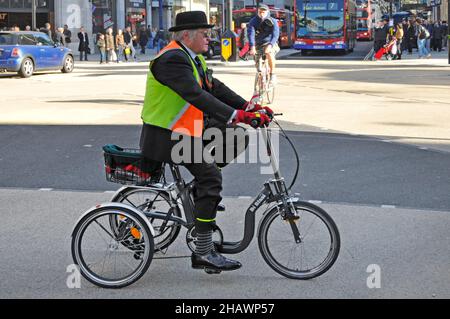 Side view city gent bowler hat wearing high visibility jacket & office suit riding Di Blasi tricycle at Oxford Circus road junction London England UK Stock Photo