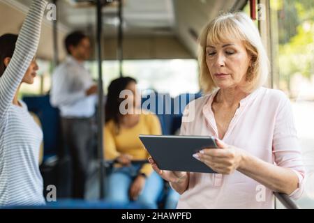 Portrait of senior woman taking bus using tablet Stock Photo
