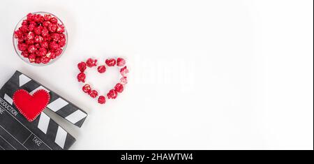 Background banner, concept of cinema on Valentine's Day. Clapperboard with heart made of red caramel popcorn with copy space on a white background. Stock Photo