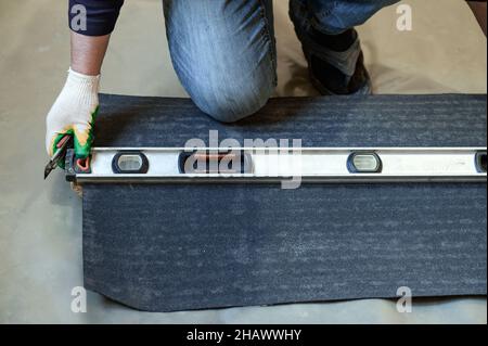 The master prepares bitumen tape for installation, protection of a floor from moisture, measurement and cutting. Stock Photo
