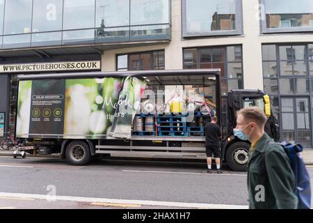 man in face mask walk past Matthew Clark delivery truck from which  delivery men unload beer barrels London Greenwich England UK Stock Photo