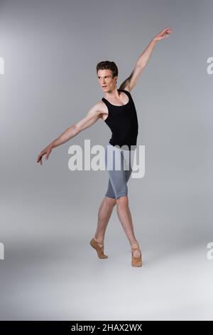 full length of young man in ballet shoes performing ballet dance on grey Stock Photo