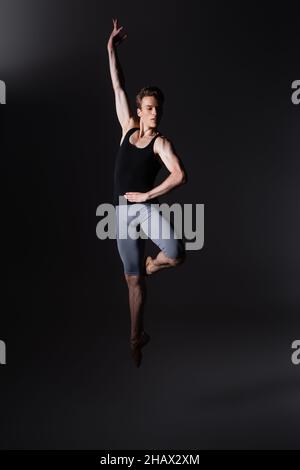 young and graceful dancer gesturing while performing ballet dance while jumping on black Stock Photo