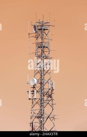 Photograph of a large steel telecommunications tower against an orange sky background Stock Photo