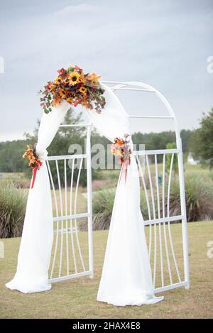 White wedding ceremony arch drapped in white cloth and decorated with sunflowers Stock Photo
