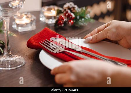 Woman serves Christmas table. Female hands hold  plate with cutlery. Table setting. Preparing for a festive dinner. Stock Photo