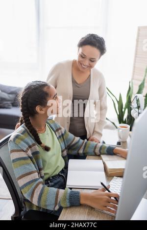 african american woman smiling near teenage daughter studying at home Stock Photo