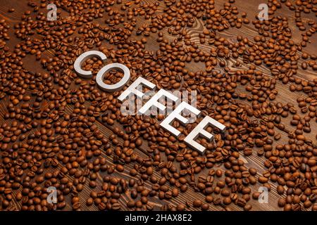 the word coffee laid with silver letters on wooden board surface covered with roasted coffee beans Stock Photo