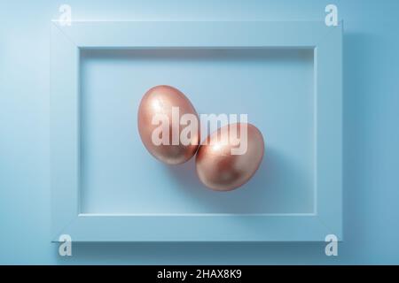 Pair of framed golden eggs on pastel blue background. Contemporary fine art easter composition. Flat lay, top view, copy space. Stock Photo