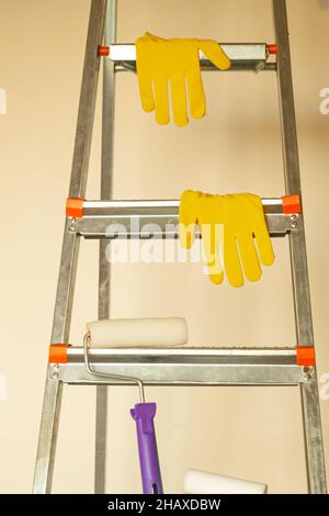The wall paint accessories lie on a stepladder against the background of an empty wall. Home renovation concept, apartment with trendy colors Stock Photo