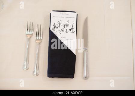 Thank you card inside of dark blue napkin with forks dinner setting Stock Photo