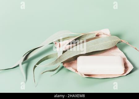 Organic soap bar on craft paper next to eucalyptus foliage on light green background Stock Photo