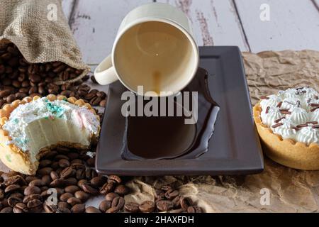 Mini white chocolate ganache pie with a bite, next to a cup of coffee overturned on brown paper (front view). Stock Photo