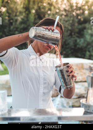 MILANP, ITALY - Nov 04, 2021: A vertical shot of a young Caucasian young female bartender making a Negroni cocktail. Stock Photo