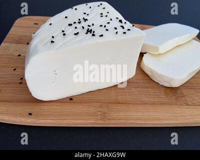 White cheese, cheese slices on a wooden plate with black background. Stock Photo