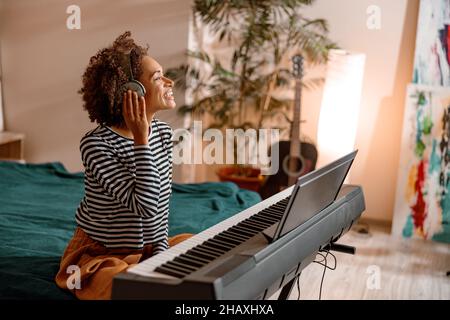 Cheerful woman in headphones playing synthesizer at home Stock Photo