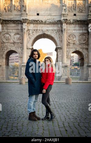 Young couple traveling to Rome. The young couple poses in front of the Arch of Titus. The blonde woman in her red jacket puts her hand on her boyfrien Stock Photo