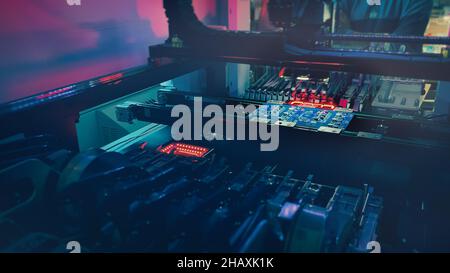 Digital technologies for automation of computer chip industry. Production of high-tech computer chips on an automatic SMT machine. Red neon lights illuminate Chip Components for automation test.  Stock Photo