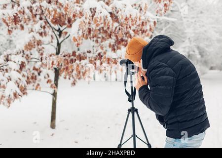 Photographer taking photos using professional digital camera on tripod in snowy winter park. Landscape pictures. Outdoor photography Stock Photo