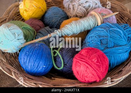 Dyed alpaca llama wool in balls with traditional knitting needles resting in wicker bowl basket at peruvian textile farm for tourists to see ancient m Stock Photo