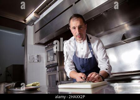 Focused male cook in apron with knife cutting fish on board while working in kitchen of restaurant Stock Photo