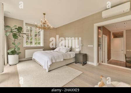 Comfortable bedroom in pastel colors with beige curtains retro armchair with plaid large bed covered with coverlet and soft carpet on laminated floor Stock Photo